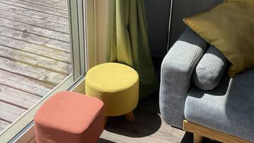 A room with a wooden floor, a grey sofa with a yellow pillow, a red ottoman, and a yellow stool.