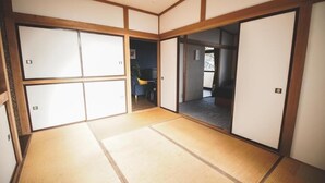 Una habitación japonesa tradicional con suelo de tatami, puertas correderas y vistas a un balcón exterior.