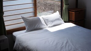 Una cama con ropa de cama blanca, cabecera de madera y una ventana con persianas.