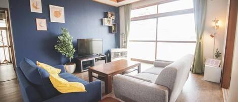 Un soggiorno con un divano blu, un divano grigio, un tavolino in legno, una televisione e una pianta in vaso.