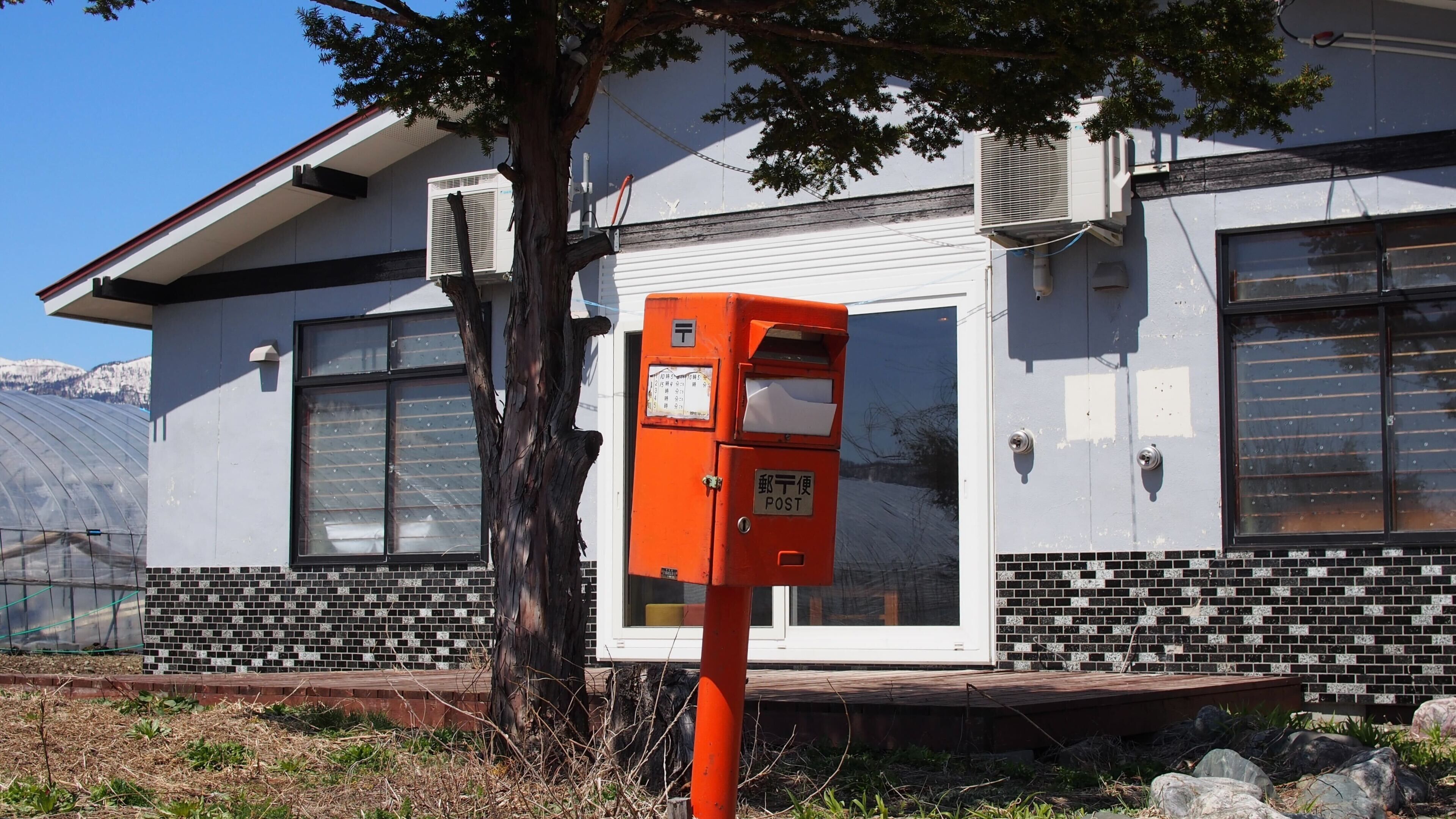 Un bâtiment avec une base en briques, de grandes fenêtres et une boîte aux lettres orange.