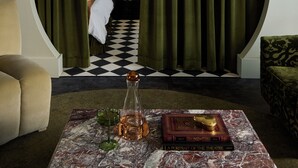A room with a checkered floor, a bed with a white cover, a table with a book and a bottle, and a green curtain. - Designed for two couples, friends or a family, flat four is one of the edgiest suites in Hotel Julie (Stratford)