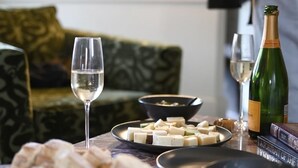 A table set with cheese, wine glasses, and a bottle of champagne, with a person in the background. - Designed for two couples, friends or a family, flat four is one of the edgiest suites in Hotel Julie (Stratford)