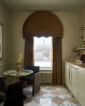 A room with a round table, chairs, a radiator, a window with curtains, and a view of the outside. - Designed for two couples, friends or a family, flat four is one of the edgiest suites in Hotel Julie (Stratford)