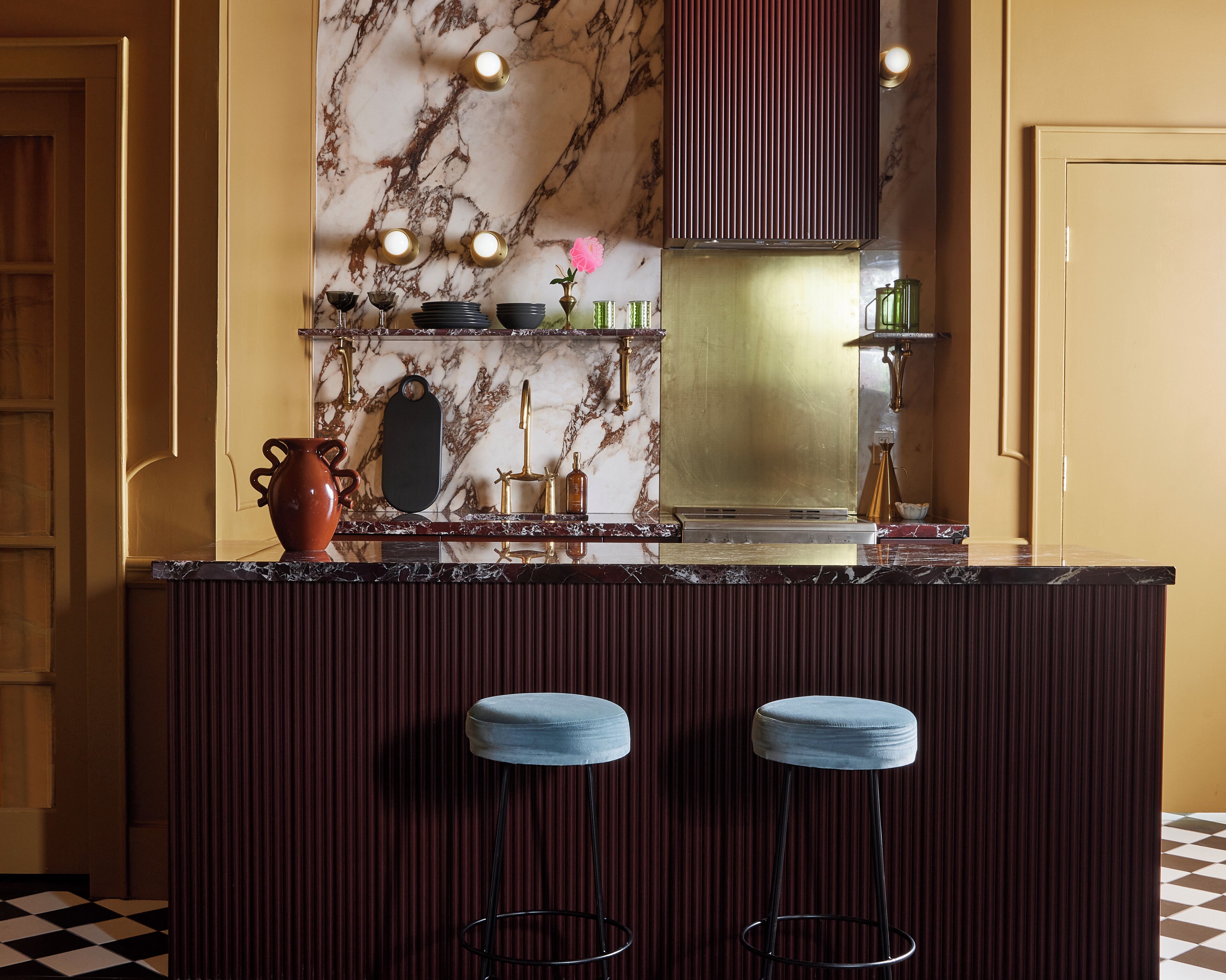 A kitchen with a marble backsplash, a built-in stove, and two bar stools.