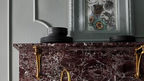 A kitchen with a marble countertop, gold faucets, and a framed artwork above the sink.