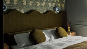 A bed with white and brown pillows, a wooden headboard, and a patterned wallpaper.