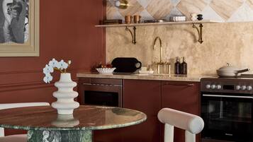 A modern kitchen with a marble countertop, a round dining table, white chairs, and a stainless steel oven.