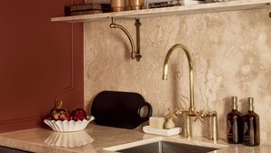 Eine Küche mit Marmor-Spritzschutz, goldenen Armaturen und einem schwarzen Topf auf der Arbeitsfläche.