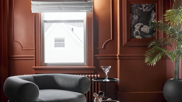 Ein modernes Wohnzimmer mit einem dunkelgrauen Sessel, einem runden Couchtisch, einer Topfpflanze und einem gerahmten Kunstwerk an der Wand.
