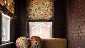 Ein Eckzimmer mit einer Bank, einem Fenster mit floralem Vorhang, einem karierten Boden und einer Ziegelwand.