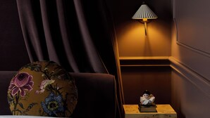 Un dormitorio con cama, mesita de noche, lámpara y cojín decorativo.