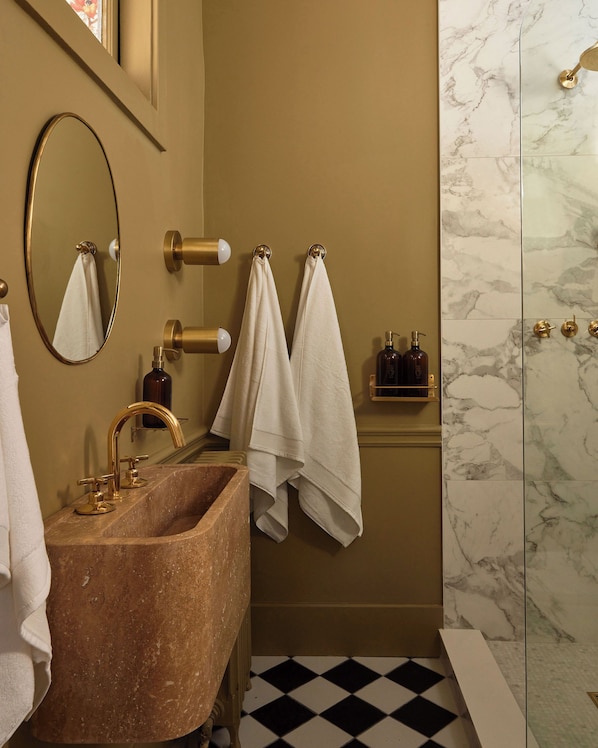 A bathroom with a marble wall, a gold sink, and two towels hanging on a towel rack.