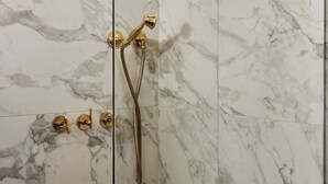 A shower with a glass enclosure and gold fixtures against a marble wall. - Designed for the solo traveller or couple looking for a taste of the Hotel Julie experience. (Stratford)