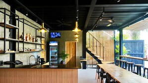 Un restaurant avec un long comptoir en bois, des étagères remplies de bouteilles et un écran de télévision.