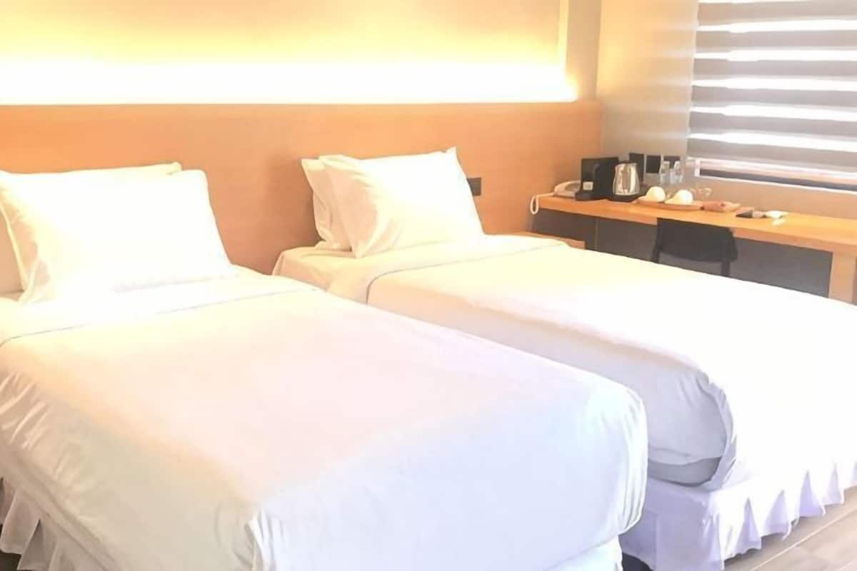 A hotel room with two beds, a desk, and a window with blinds.