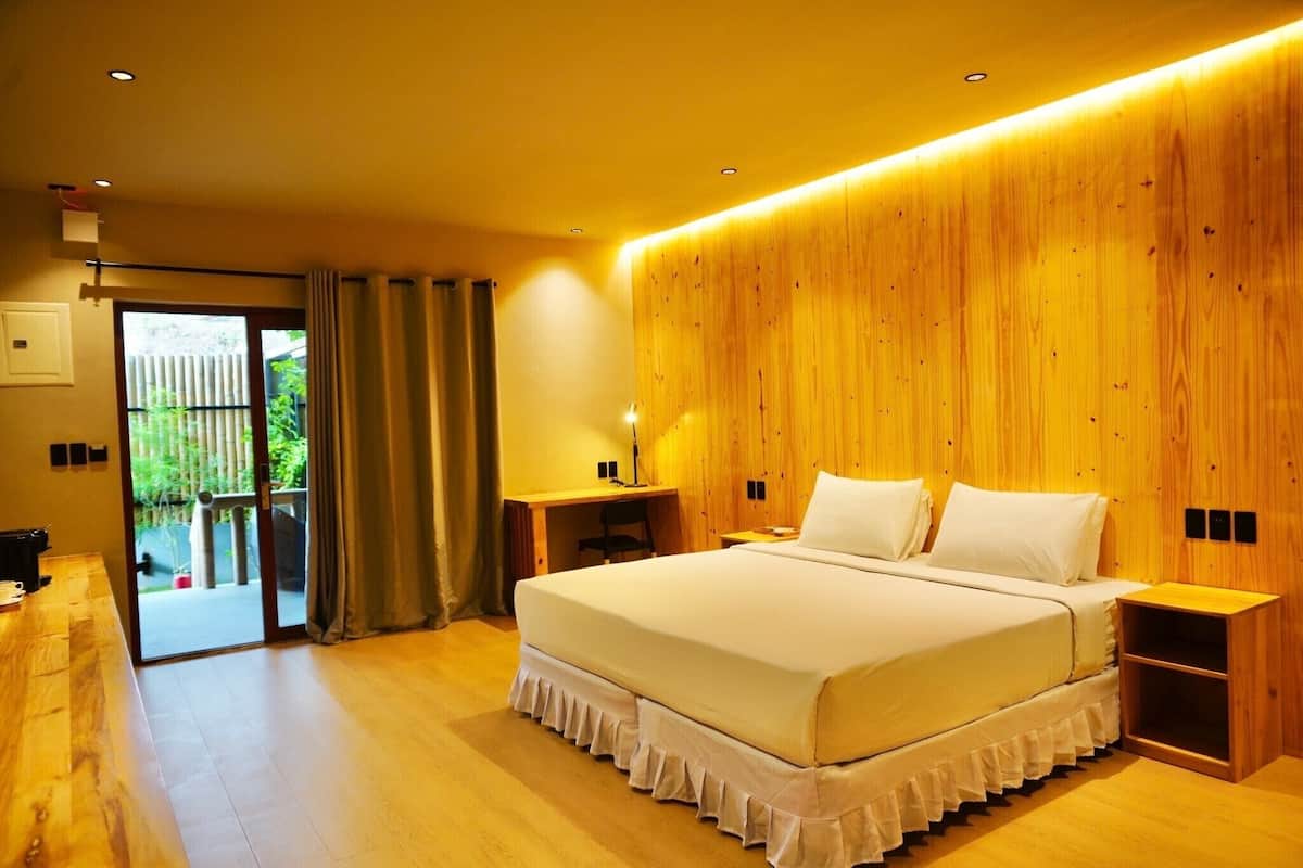 A modern bedroom with a large bed, wooden panel walls, a desk, and a sliding glass door to an outdoor area.