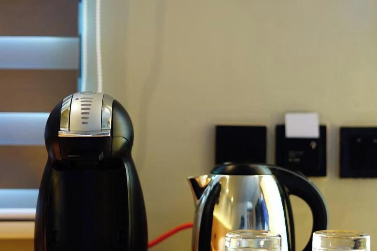 A modern kitchen with a black electric kettle and a stainless steel coffee pot on the counter.