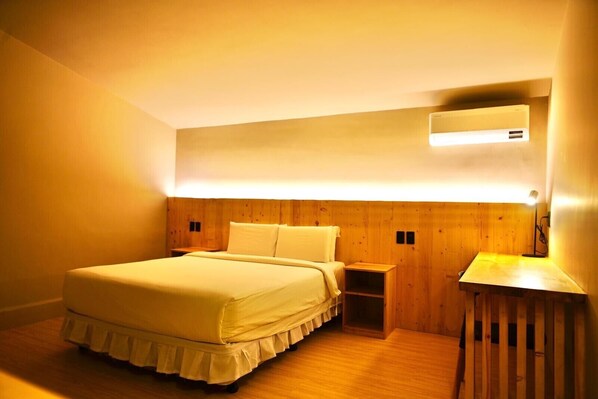 A bedroom with a bed, bedside tables, a desk, and an air conditioning unit.