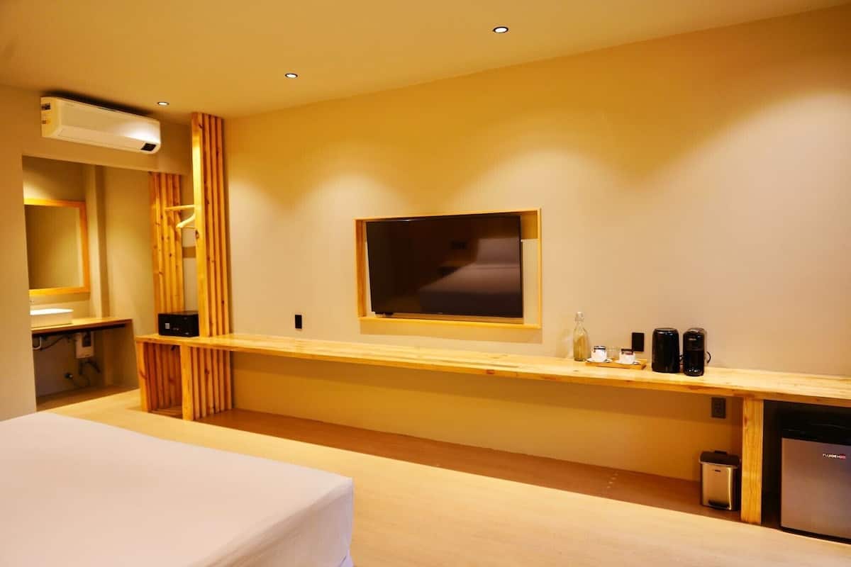 A modern hotel room with a large bed, a wooden desk, a flat-screen TV mounted on the wall, and a built-in coffee machine.