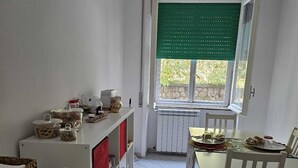 A compact kitchen with a dining area, featuring a window with green blinds, a white refrigerator, and a table set for two.