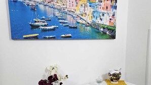 A white console table with a framed coastal town painting, a vase with flowers, a book, and decorative items.
