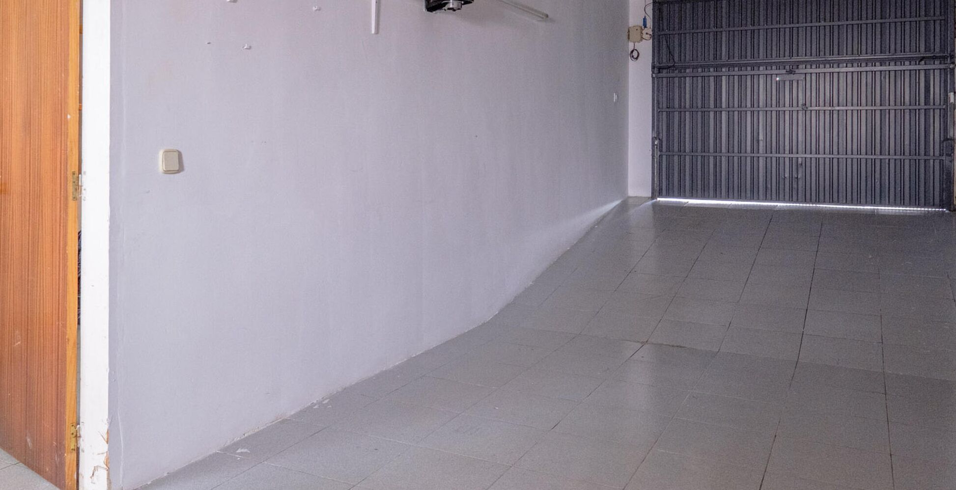 Un pasillo con piso de baldosas, una puerta metálica cerrada y un marco de puerta de madera.