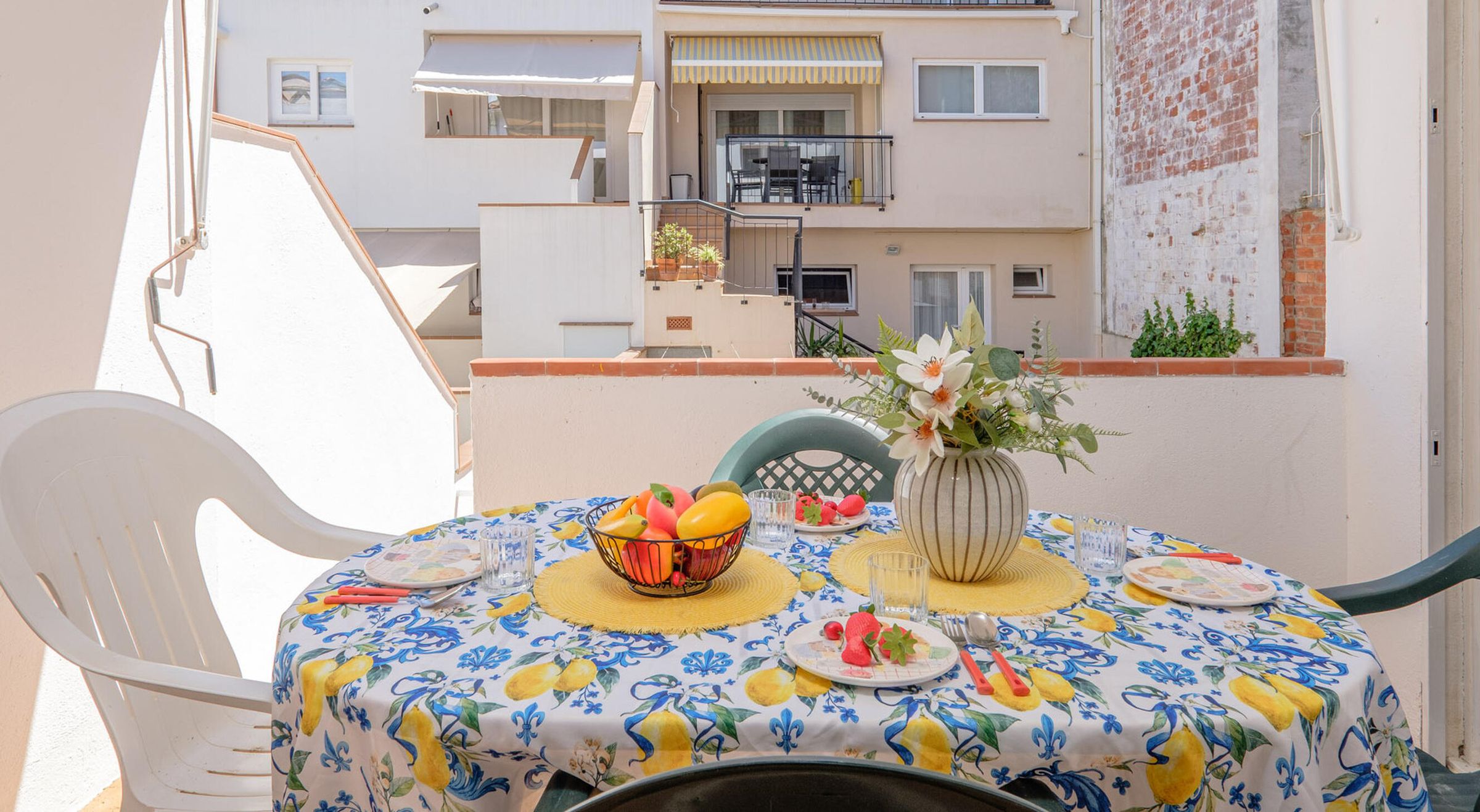 Un balcon avec une table dressée pour le repas, une chaise et un pot de fleurs.