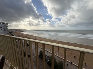 A beach with a promenade, buildings in the background, and a cloudy sky.