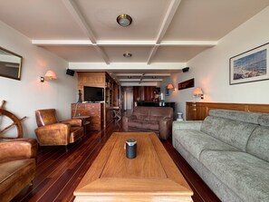 A spacious living area with a wooden coffee table, leather sofas, and a television on a cabinet.