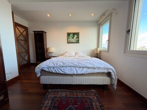 A bedroom with a bed, a nightstand, a lamp, a painting, and a window.