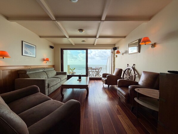 A spacious living area with a sofa, armchairs, a coffee table, and a view of the sea through a large sliding door.