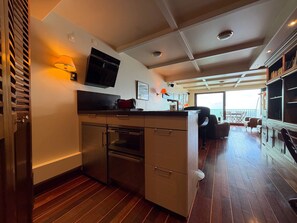 A modern kitchen with a built-in oven, a flat-screen TV, and a dining area with a view of the sea.