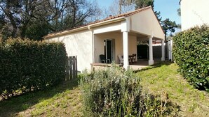 A covered patio with outdoor furniture, a white building with a tiled roof, and surrounding greenery. - Cozy apartment with private garden, near beach, perfect for couples (Saint-Brevin-les-Pins)
