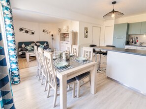 Una cucina moderna con mobili bianchi, un'area pranzo con tavolo e sedie in legno, e un soggiorno con divano e cuscini.