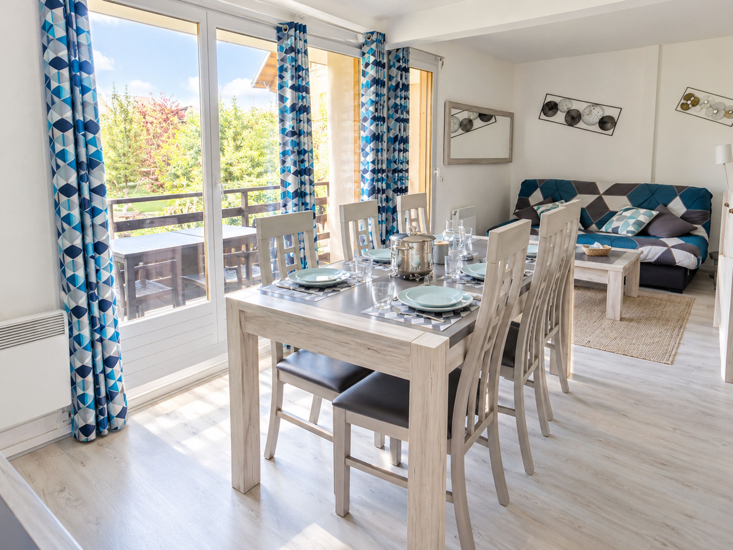 A dining area with a table set for four, chairs, a sofa, and a view through a glass door to the outdoors.