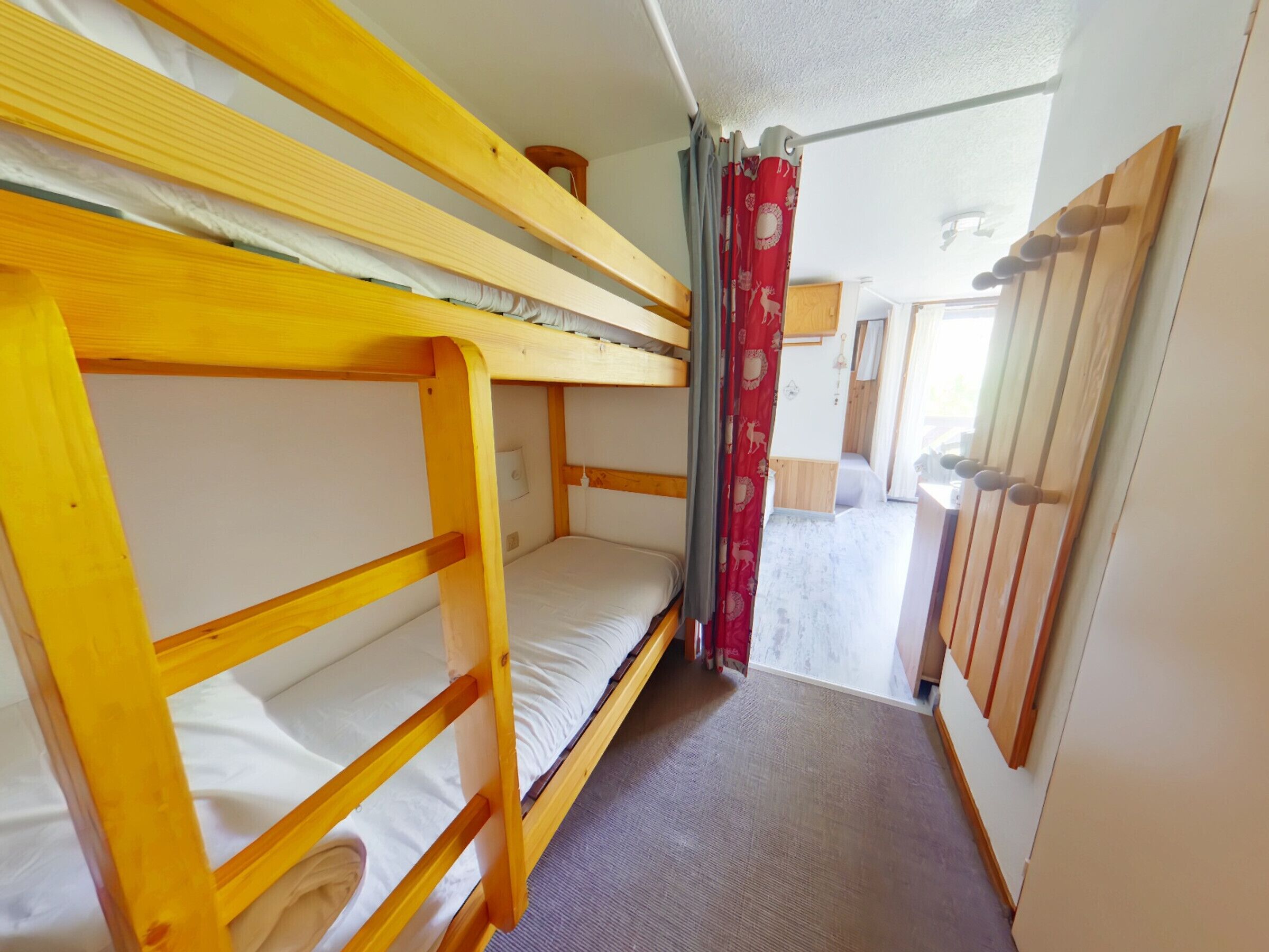 A bunk bed room with a wooden floor, a small window, and a curtain.