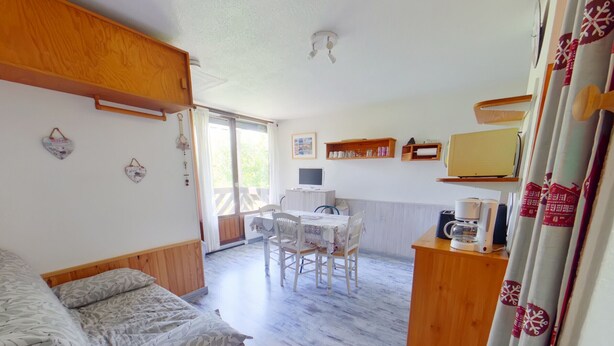 A cozy room with a bed, a dining table, chairs, a small kitchen area, and a sliding glass door leading to an outdoor deck. - Bright studio with loggia and parking in Les Rousses (Les Rousses)