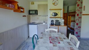 A compact kitchen with a microwave, toaster, and coffee maker. A dining table with chairs is in the center. - Bright studio with loggia and parking in Les Rousses (Les Rousses)