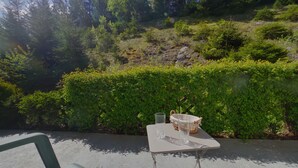 Une table avec un panier et un verre, placée devant un décor de feuillage verdoyant et une colline rocheuse.