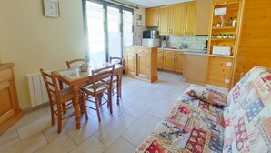 Une cuisine compacte avec des meubles en bois, une table à manger avec des chaises, un canapé avec une courtepointe et une fenêtre avec des stores.