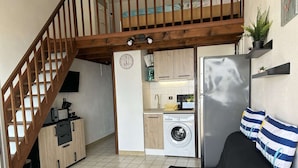 Eine kompakte Küche mit Waschmaschine, ein Essbereich mit schwarzem Sofa und eine Holztreppe.