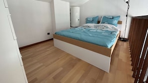 Ein Schlafzimmer mit Bett, Holzboden, weißen Wänden und einem Oberlicht.