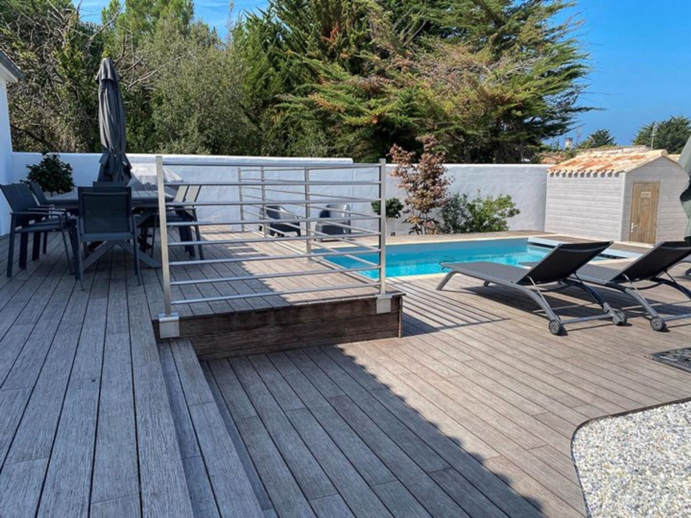 Een houten terras met een zwembad, ligbedden en een tafel met stoelen.
