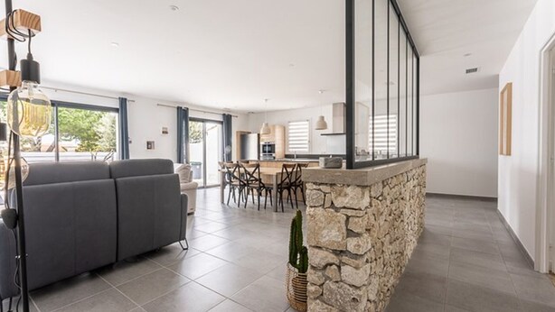 A spacious living area with a grey sofa, a dining table with chairs, a kitchen area, and a stone accent wall. - 125m² Villa with Heated Pool, 3 Bedrooms, Terrace in La Flotte (La Flotte)
