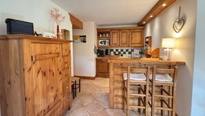 A kitchen with wooden cabinets, a tiled floor, a dining table with chairs, and a microwave. - Charming 3-room apartment in Méribel Village with parking and WIFI (Méribel)