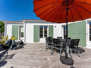 Eine Terrasse mit Tisch, Stühlen und Sonnenschirm, sowie ein Gebäude mit grünen Fensterläden.
