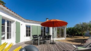 Una terraza de madera con una mesa, sillas, un paraguas rojo y un cerramiento de vidrio.