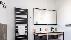 Un baño moderno con un perchero negro, un espejo sobre un tocador blanco y un mueble de madera debajo.