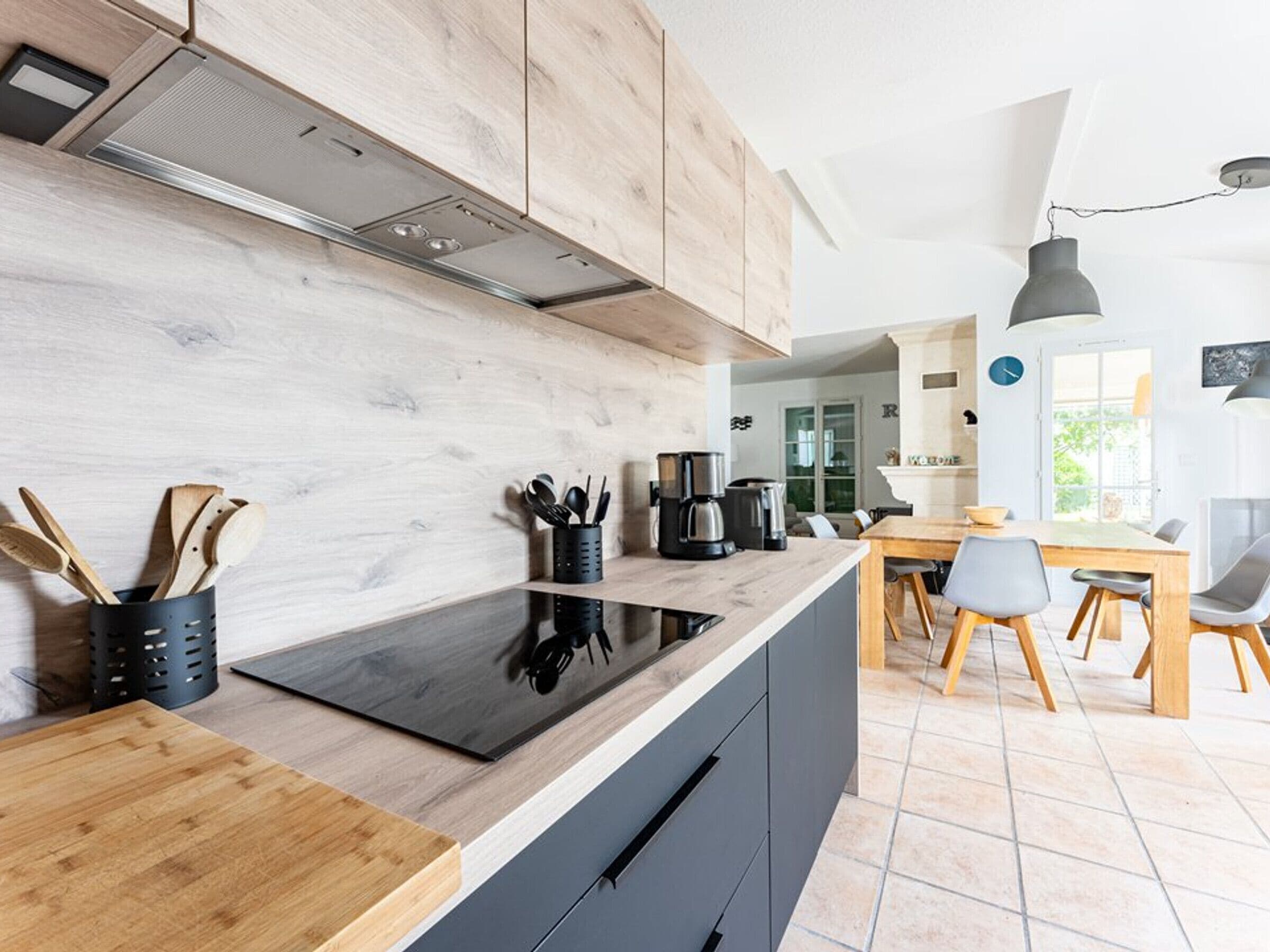 A modern kitchen with wooden cabinets, a black countertop, and a dining area with a wooden table and chairs.